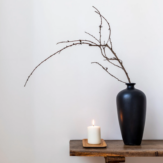 burning white candle with tall black vase containing a single branch